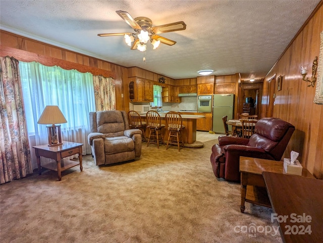 living room with light carpet, ceiling fan, a textured ceiling, and wood walls