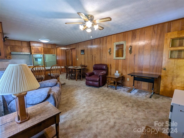 carpeted living room featuring ceiling fan, a textured ceiling, and wood walls