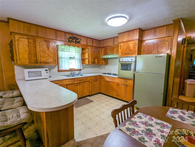 kitchen with sink, a textured ceiling, white appliances, and kitchen peninsula