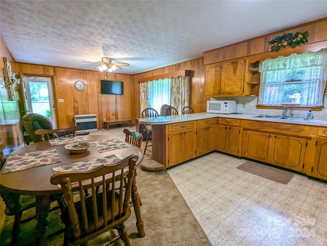 kitchen with sink, a textured ceiling, wooden walls, kitchen peninsula, and ceiling fan