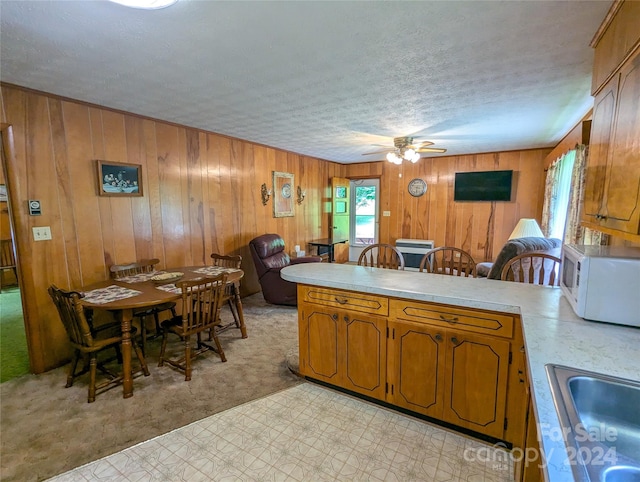 kitchen with sink, ceiling fan, a textured ceiling, kitchen peninsula, and wood walls