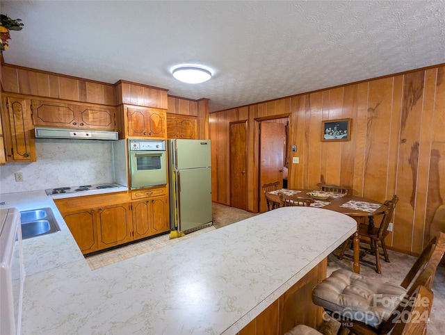 kitchen featuring white cooktop, sink, wood walls, stainless steel refrigerator, and oven