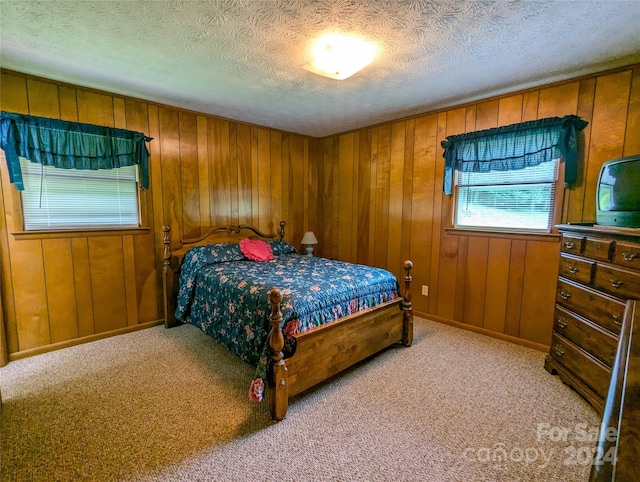 bedroom featuring light colored carpet, a textured ceiling, and wood walls