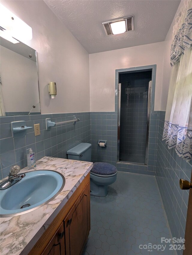 bathroom with tile patterned floors, a shower with door, tile walls, and a textured ceiling