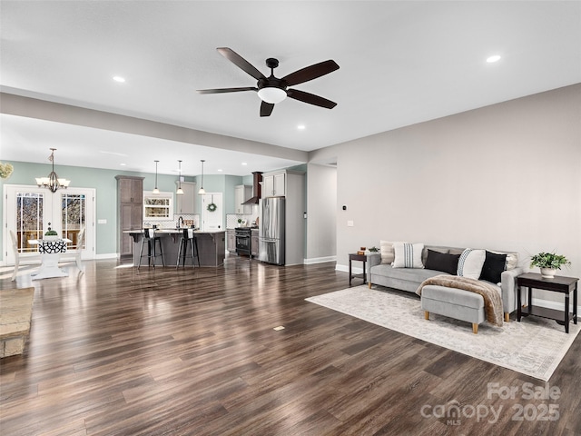 living area featuring recessed lighting, dark wood finished floors, baseboards, and ceiling fan with notable chandelier