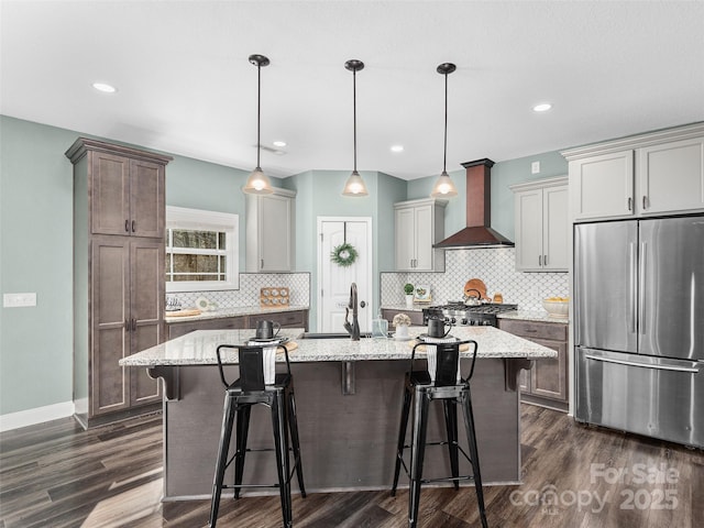 kitchen with stainless steel fridge, dark wood finished floors, an island with sink, wall chimney range hood, and a sink