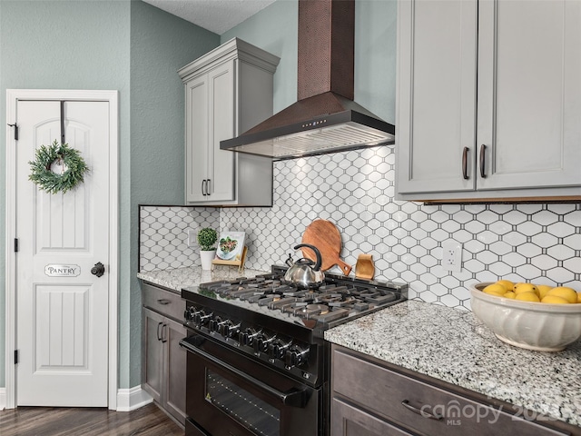 kitchen featuring dark wood-style floors, light stone counters, backsplash, high end black range, and wall chimney exhaust hood