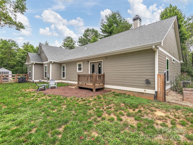 back of property with roof with shingles, a chimney, a lawn, fence, and a deck