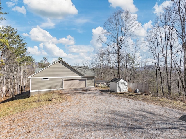 view of side of property featuring an outbuilding, a garage, fence, a shed, and gravel driveway