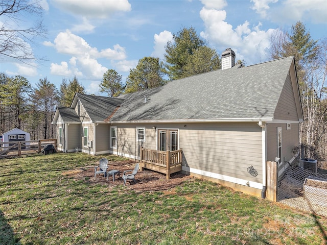 rear view of property featuring a chimney, roof with shingles, a lawn, and a deck