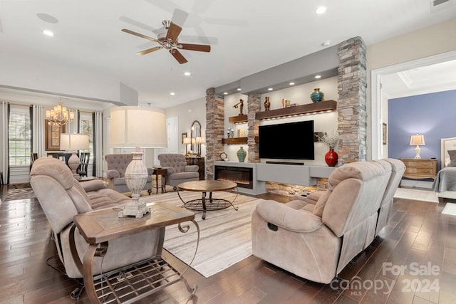 living room featuring dark hardwood / wood-style flooring, ceiling fan with notable chandelier, and a stone fireplace