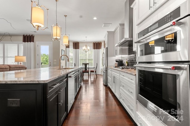 kitchen featuring sink, appliances with stainless steel finishes, a spacious island, decorative light fixtures, and wall chimney exhaust hood