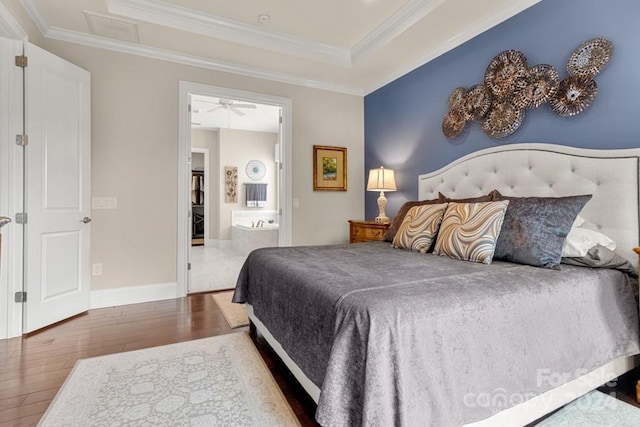 bedroom featuring a tray ceiling, crown molding, hardwood / wood-style flooring, and ensuite bathroom