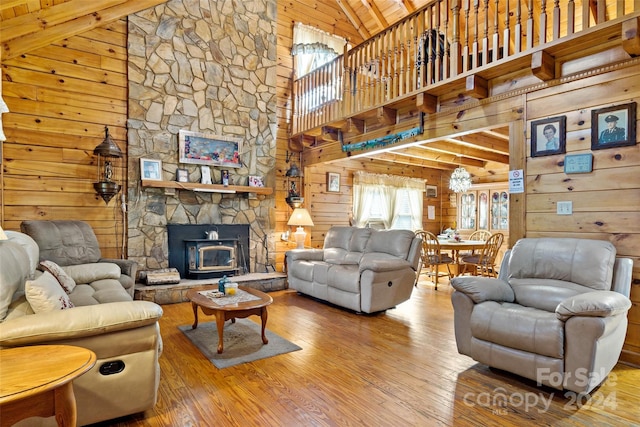 living room featuring hardwood / wood-style floors, wooden walls, a wood stove, and high vaulted ceiling