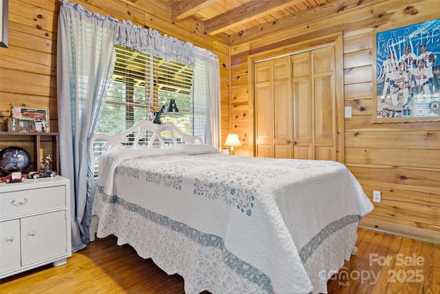 bedroom with beamed ceiling, wood walls, wooden ceiling, and wood finished floors