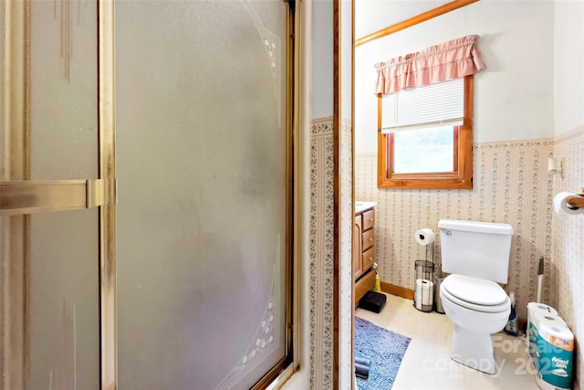 bathroom with wallpapered walls, a shower stall, toilet, and wainscoting