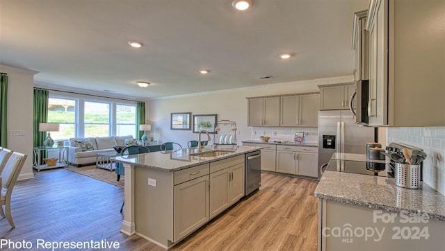 kitchen with appliances with stainless steel finishes, an island with sink, sink, gray cabinetry, and light stone counters