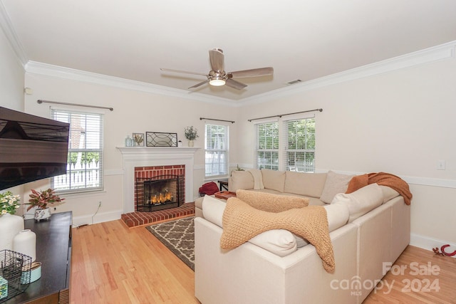 living room with ceiling fan, crown molding, light wood-type flooring, and a brick fireplace