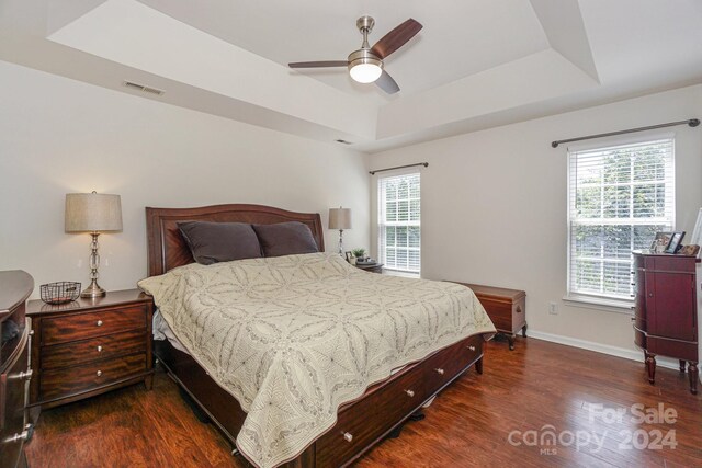 bedroom with ceiling fan, a raised ceiling, and dark wood-type flooring