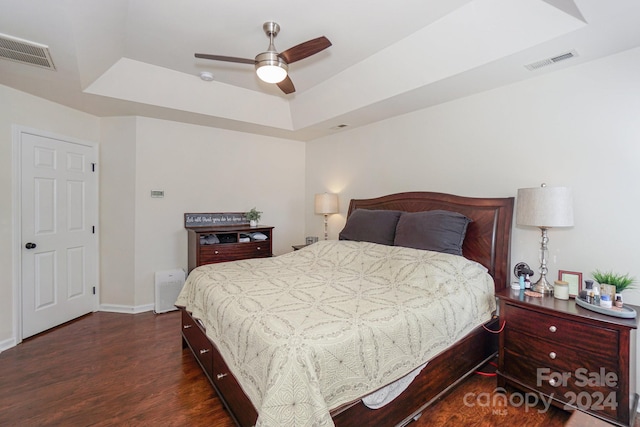 bedroom featuring ceiling fan, dark hardwood / wood-style floors, and a tray ceiling