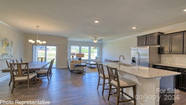 kitchen with hanging light fixtures, dark wood-type flooring, a sink, an island with sink, and stainless steel fridge