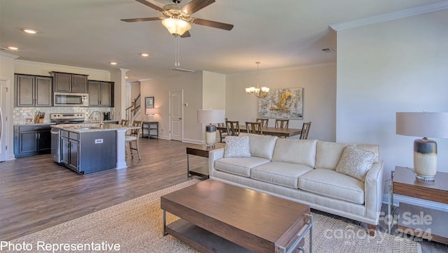 living area featuring visible vents, dark wood-style flooring, ceiling fan with notable chandelier, crown molding, and recessed lighting