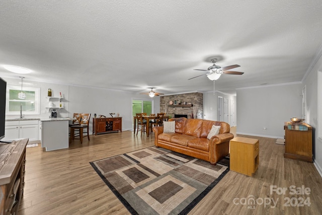 living room featuring sink, a large fireplace, a textured ceiling, and light wood-type flooring