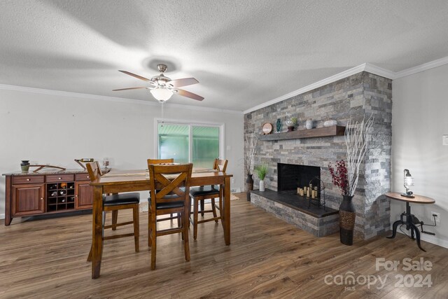 dining room featuring a textured ceiling, dark wood-type flooring, ceiling fan, a fireplace, and ornamental molding