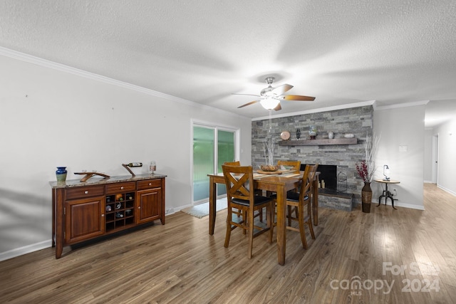 dining area with crown molding, dark wood-type flooring, ceiling fan, a fireplace, and a textured ceiling