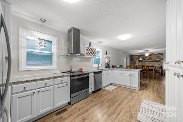 kitchen featuring stainless steel appliances, white cabinets, decorative light fixtures, kitchen peninsula, and wall chimney exhaust hood