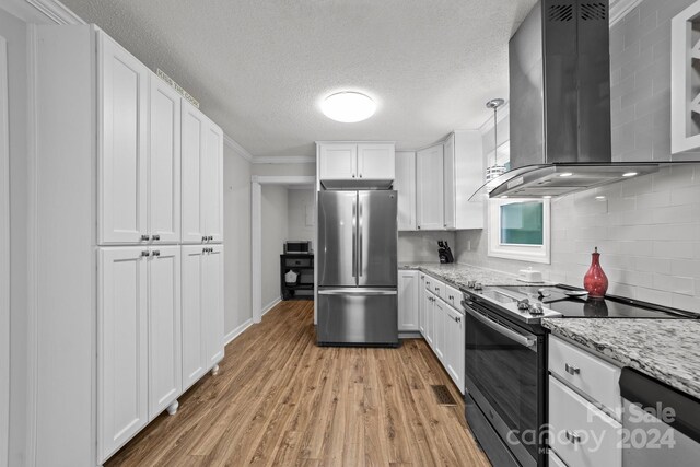 kitchen featuring light hardwood / wood-style flooring, wall chimney range hood, white cabinets, backsplash, and appliances with stainless steel finishes