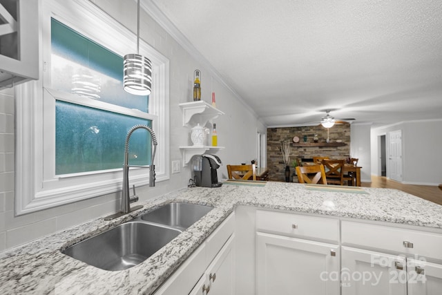 kitchen featuring white cabinetry, sink, ceiling fan, crown molding, and a textured ceiling