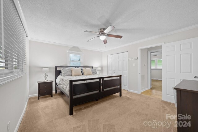 bedroom with a closet, a textured ceiling, light carpet, ceiling fan, and ornamental molding