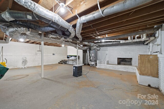 basement featuring brick wall, heating unit, and a fireplace