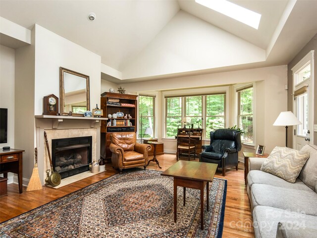 living room with a skylight, light hardwood / wood-style flooring, a fireplace, and high vaulted ceiling