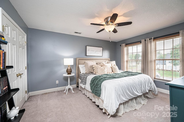 bedroom with a textured ceiling, ceiling fan, a closet, and light colored carpet