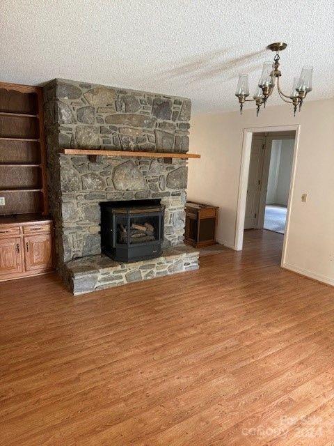 unfurnished living room with a textured ceiling, a notable chandelier, a fireplace, and hardwood / wood-style flooring