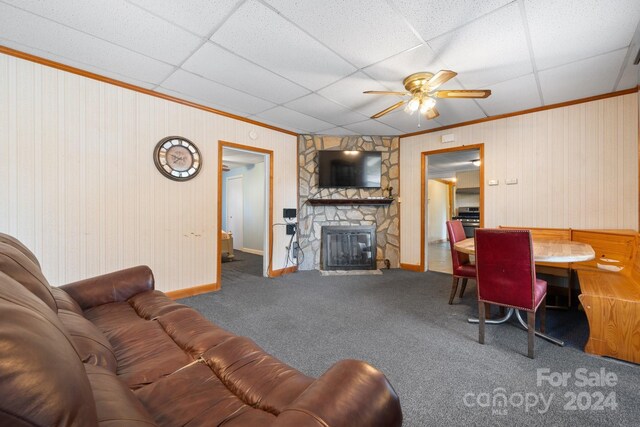 carpeted living room featuring a stone fireplace, a paneled ceiling, and ceiling fan