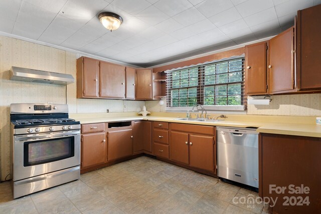 kitchen with crown molding, light tile patterned floors, stainless steel appliances, wall chimney exhaust hood, and sink