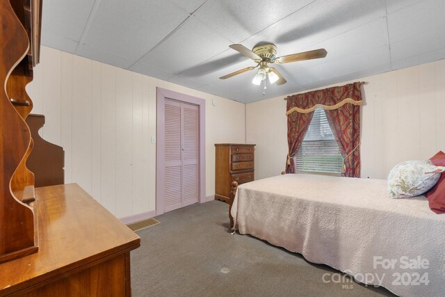 bedroom with carpet floors, ceiling fan, a drop ceiling, and a closet