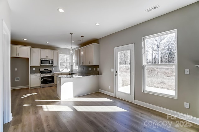 kitchen featuring appliances with stainless steel finishes, decorative light fixtures, white cabinetry, backsplash, and kitchen peninsula