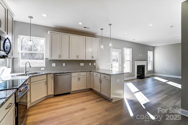 kitchen featuring light hardwood / wood-style floors, kitchen peninsula, appliances with stainless steel finishes, tasteful backsplash, and hanging light fixtures