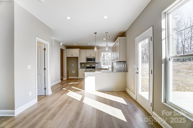 kitchen with stainless steel appliances, plenty of natural light, hanging light fixtures, light hardwood / wood-style flooring, and light stone counters