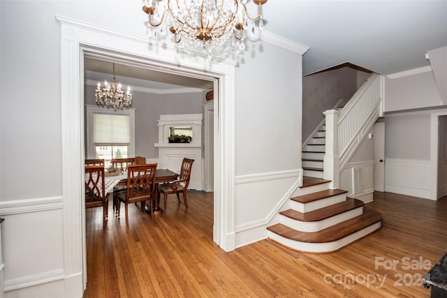 stairs with an inviting chandelier, ornamental molding, and hardwood / wood-style floors