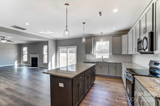 kitchen featuring appliances with stainless steel finishes, pendant lighting, light stone counters, and a kitchen island