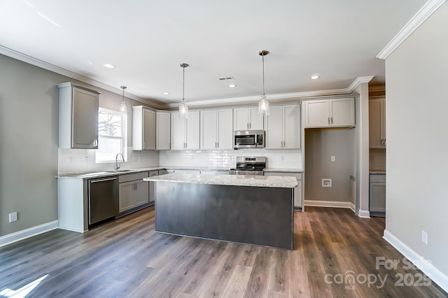 kitchen with pendant lighting, a kitchen island, sink, ornamental molding, and stainless steel appliances