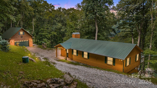 view of front facade with a garage, faux log siding, a chimney, an outdoor structure, and a wooded view