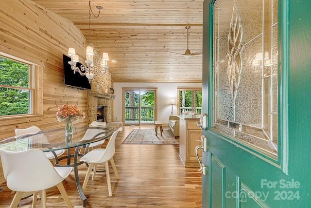 dining area with wood ceiling, wood finished floors, a stone fireplace, a healthy amount of sunlight, and wood walls