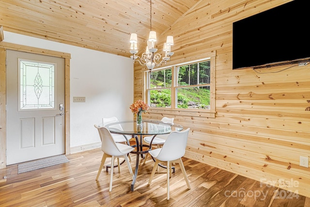 dining area featuring an inviting chandelier, wooden walls, vaulted ceiling, and light wood finished floors