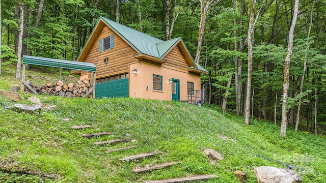 view of side of home featuring a garage, a forest view, metal roof, and stucco siding